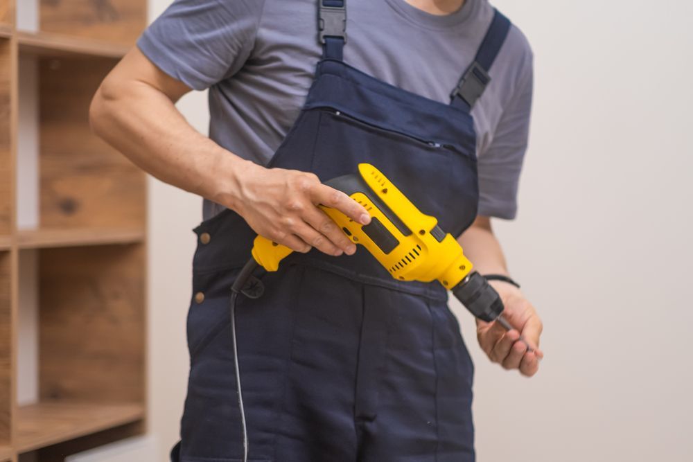 Un hombre con un mono azul sostiene un taladro amarillo.