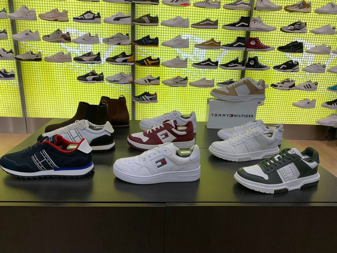 Un mur d'exposition de baskets avec des chaussures de sport colorées sur des étagères et une table de chaussures devant.