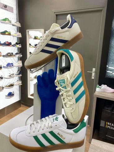 Trois baskets Adidas à rayures bleues, turquoise et vertes présentées sur un présentoir dans un magasin de chaussures.
