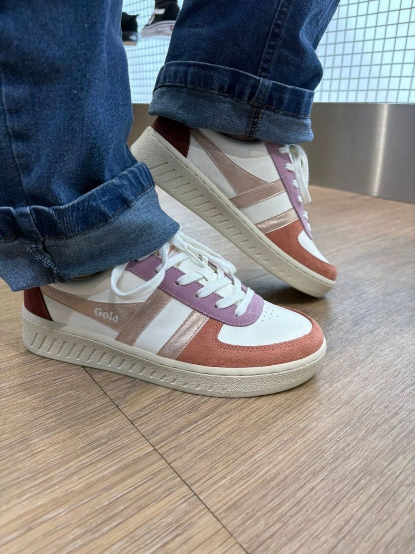Gros plan sur des pieds chaussés de baskets multicolores et de jeans, debout sur un parquet.