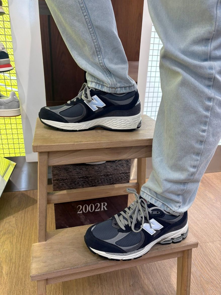 Une personne portant des baskets noires se tient debout sur un petit tabouret en bois à l'intérieur.