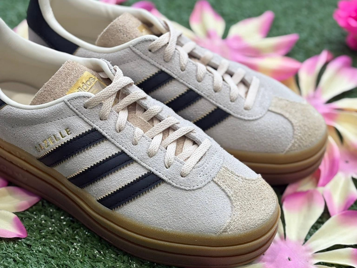 Une paire de baskets Adidas beiges à rayures noires sur l'herbe à côté de fleurs roses