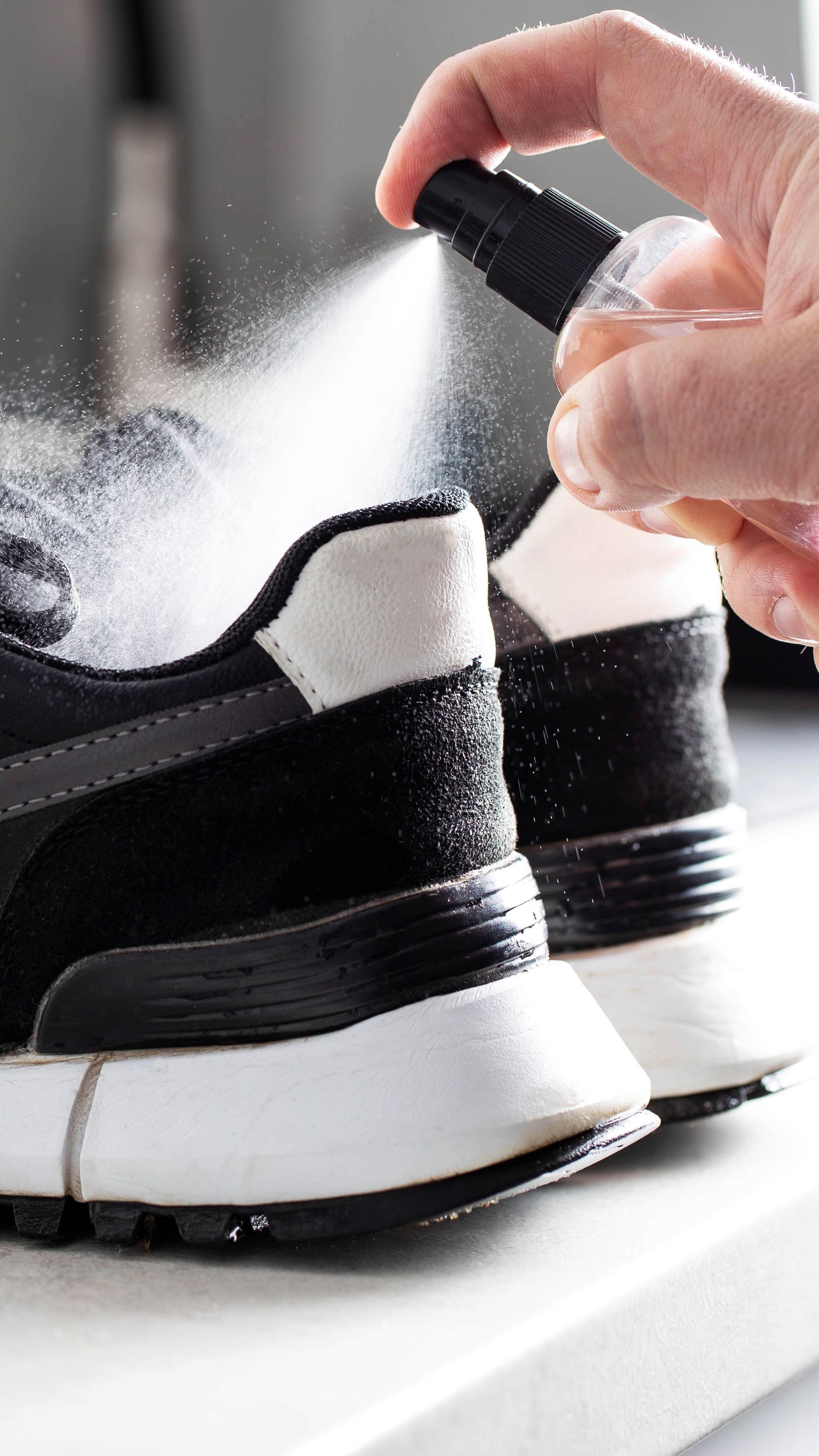 Pulvérisation manuelle d'une solution nettoyante sur des baskets noires et blanches posées sur une surface blanche