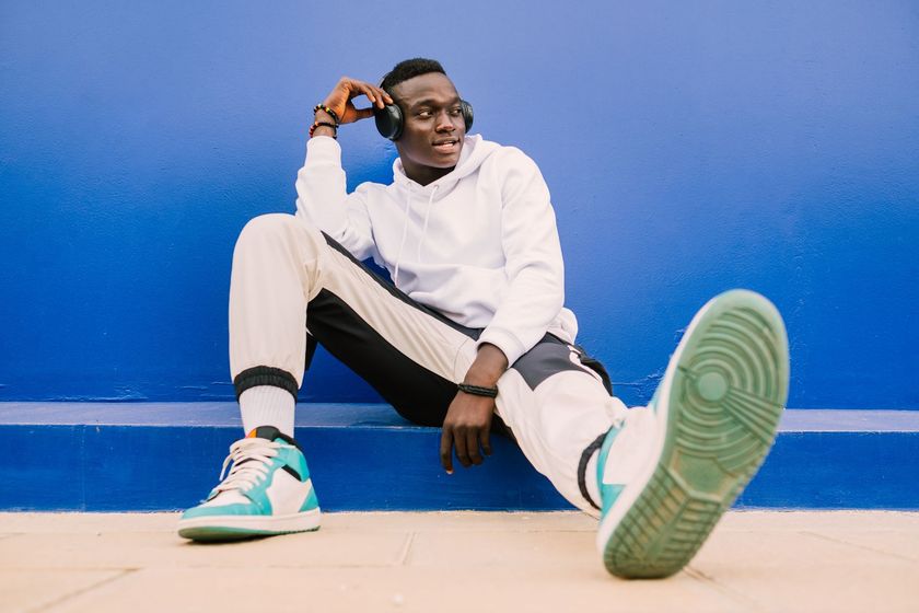 Personne assise contre un mur bleu, vêtue de vêtements blancs et noirs et de baskets turquoise.
