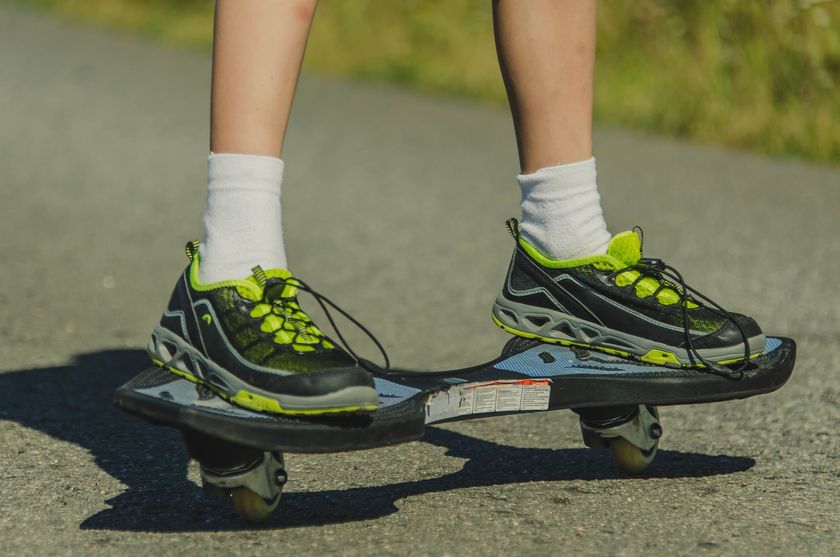 Des pieds chaussés de baskets vert fluo et noires sur un skateboard, roulant sur une piste pavée.