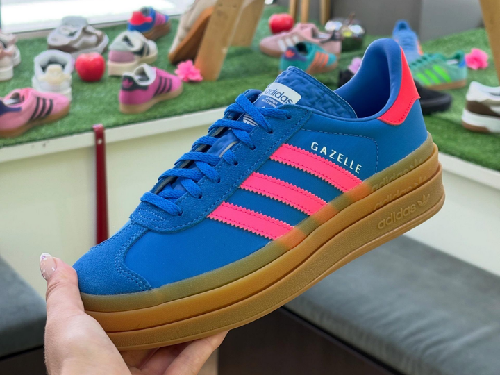 Baskets Adidas Gazelle bleues à rayures roses et semelle en gomme, tenues à la main à l'extérieur