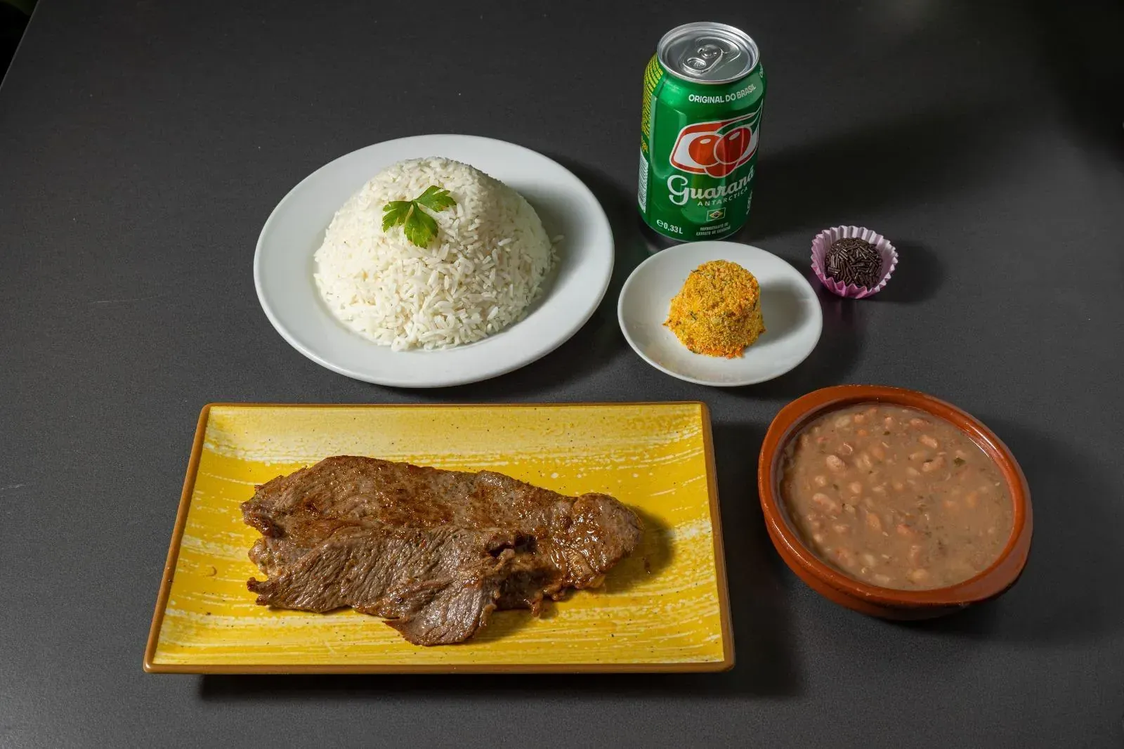 Comida con bistec, arroz y pequeños cuencos de condimentos en una mesa.