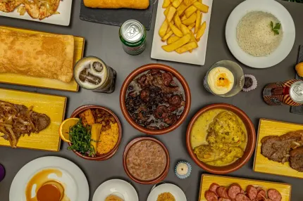 Una mesa con plato brasileño de feijoada, que incluye frijoles, salchichas, guarniciones y una rodaja de naranja.