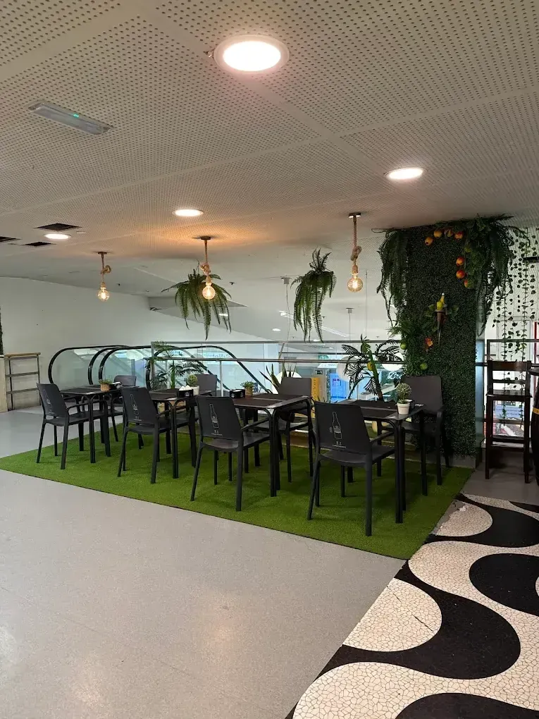 Zona de estar del restaurante con mesas, sillas negras y césped artificial en el suelo, junto a una escalera mecánica.