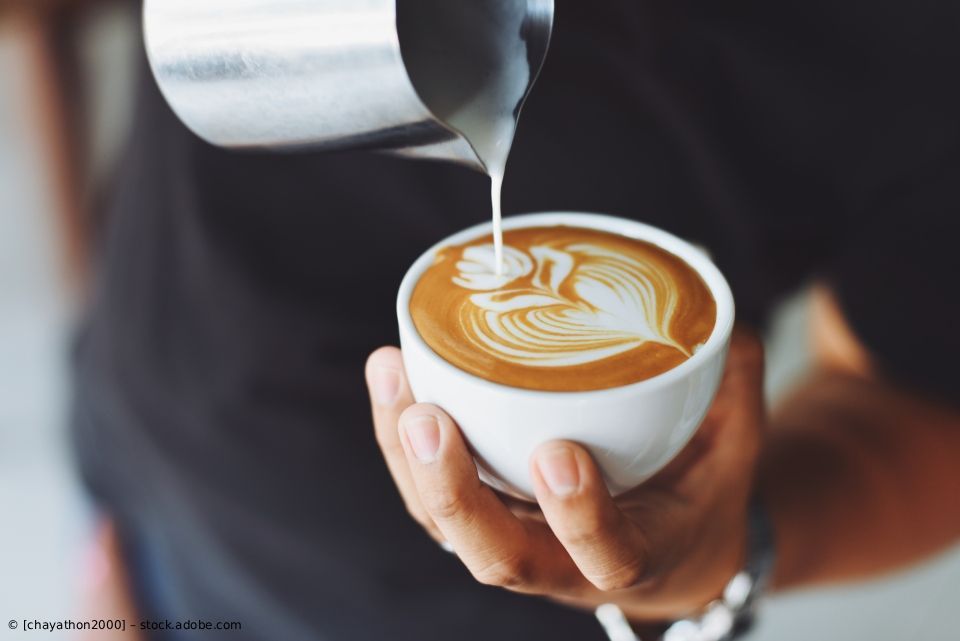 Ein Barista gießt aufgeschäumte Milch in eine Tasse Latte mit herzförmiger Latte Art.