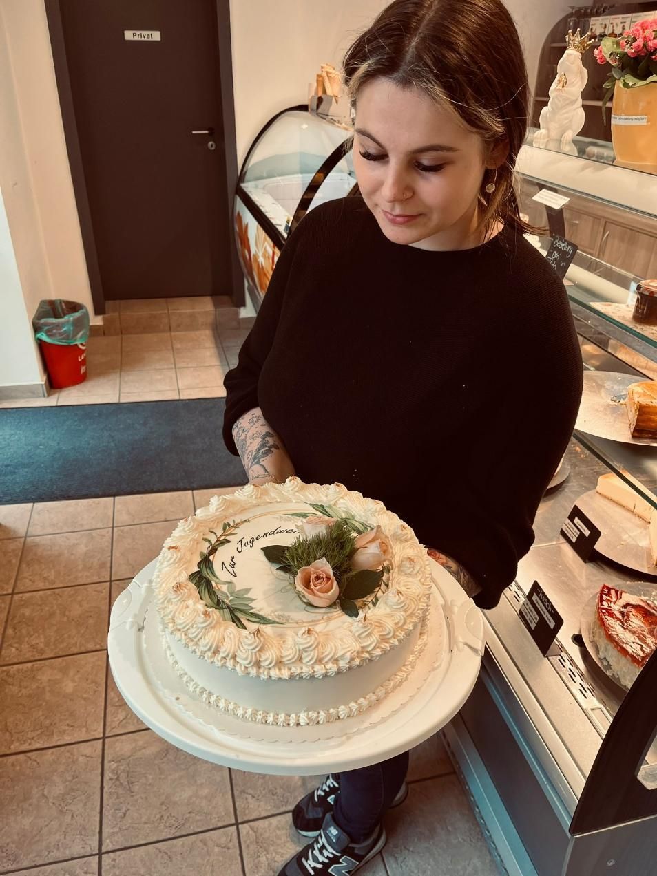Frau hält einen weiß glasierten Kuchen in einem Bäckereiregal.