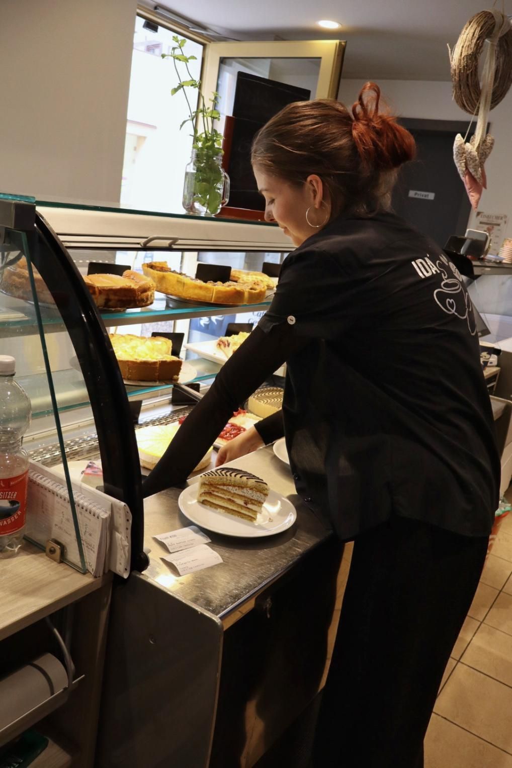 Ein Mitarbeiter arrangiert Gebäck in einer Bäckereiauslage.