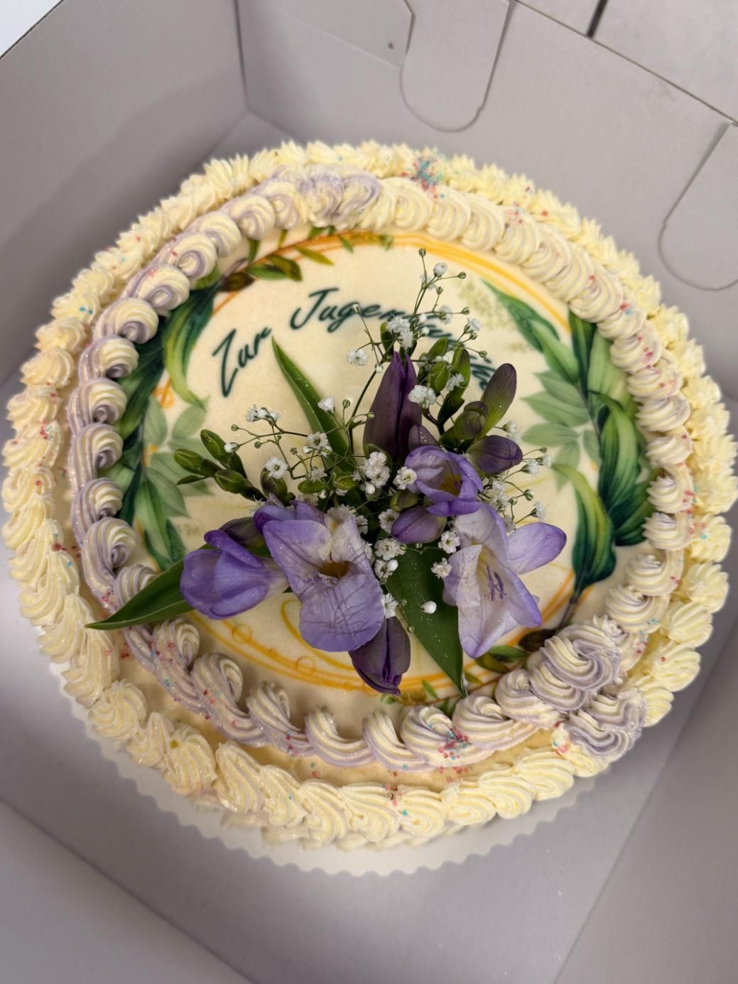 Runder weißer Kuchen mit floralem Zuckerguss und lila Blüten, dekoriert zum ersten Jahrestag in Japan.