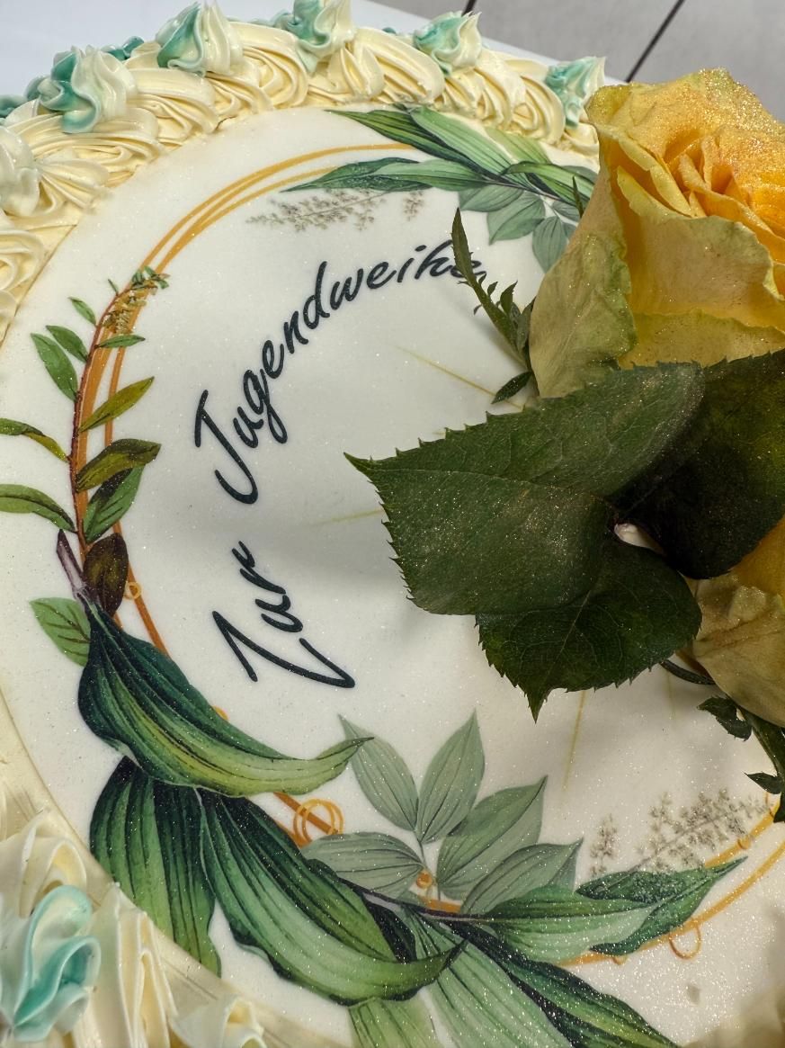Dekorativer weißer Kuchen mit gelben Rosen, grünen Blättern und deutschem Text obenauf