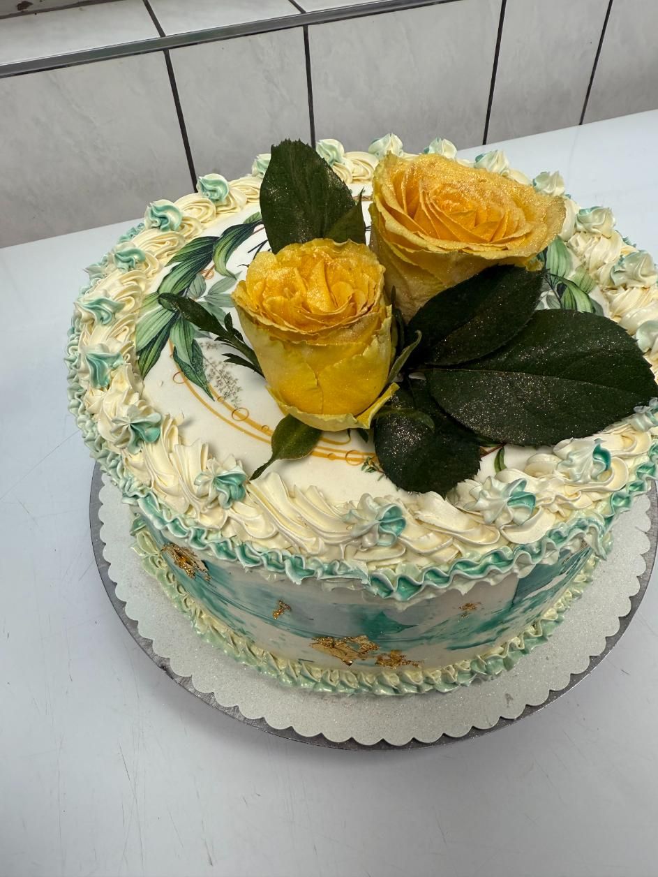 Verzierter weißer Kuchen mit gelben Rosen und grünen Blättern auf einem weißen Kuchenbrett