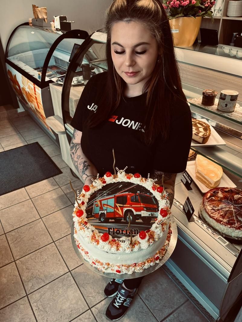 Frau hält eine verzierte Torte in einem Auslagebereich einer Bäckerei