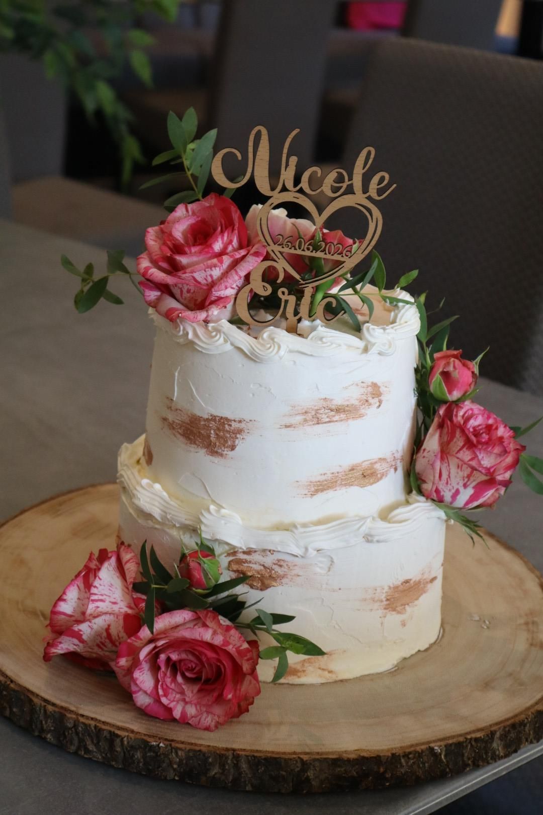Zweistöckige weiße Torte mit rosa Rosen und goldenem „Nicole“-Schriftzug auf einer Holzplatte