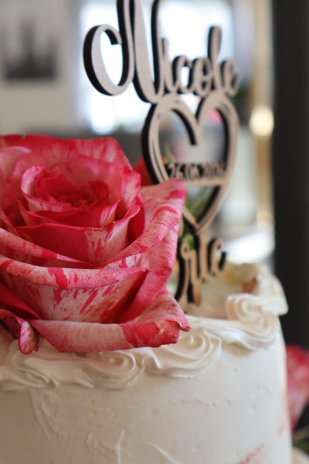 Weißer Kuchen mit rosa Rose und schwarzem „Miche…“-Schriftzug auf einem dekorierten Desserttisch