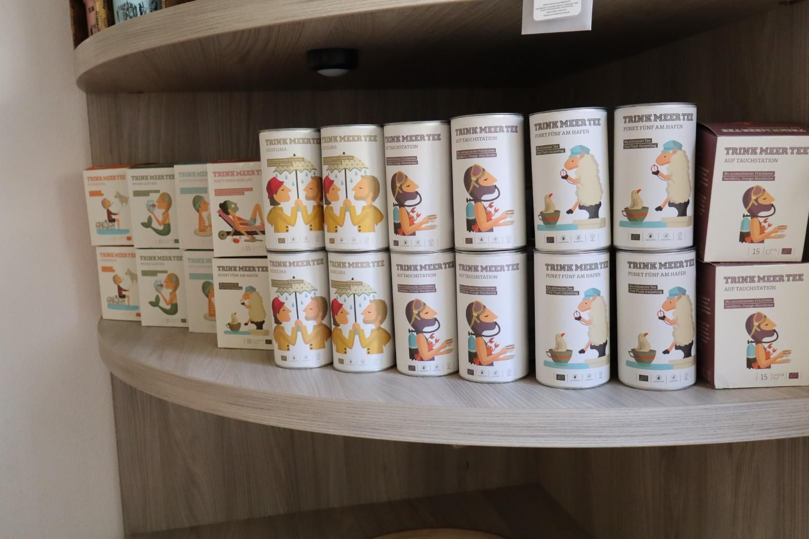 Eine Reihe kleiner, illustrierter Produktgläser steht auf einem gebogenen Holzregal in einem Laden oder Schrank.
