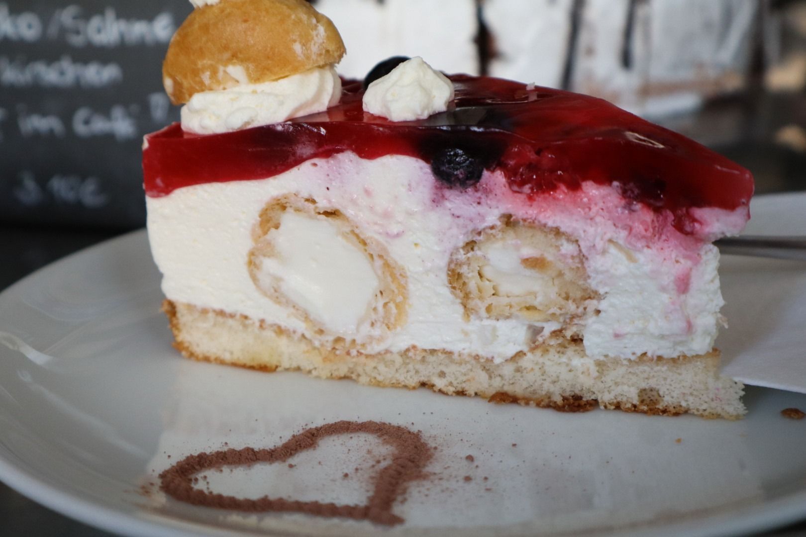Ein Stück Schichttorte mit roten Beeren und Sahnefüllung auf einem weißen Teller