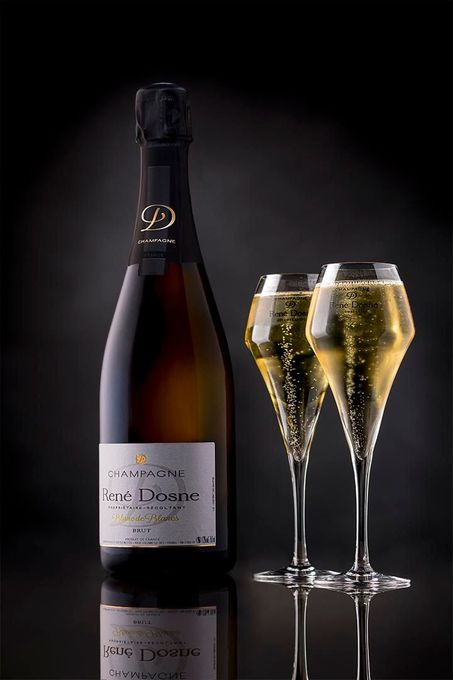 Bouteille de champagne à côté de deux flûtes remplies sur une surface noire réfléchissante.