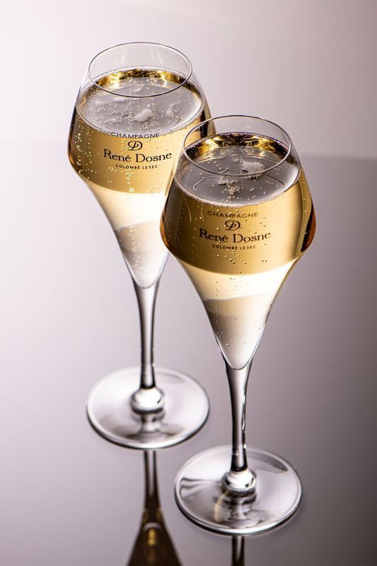 Deux flûtes à champagne remplies de vin blanc pétillant posées sur une surface réfléchissante.
