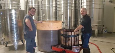 Deux personnes se tiennent à côté d'une grande cuve métallique dans une brasserie, avec des cuves en acier inoxydable en arrière-plan.