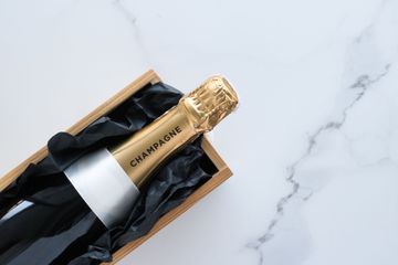 Bouteille de champagne dans un étui noir orné de dorures, présentée dans un coffret en bois sur une surface en marbre.