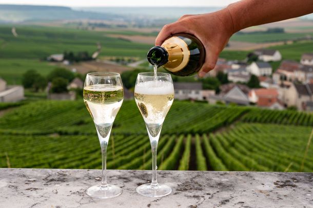 Verser à la main du vin mousseux dans deux flûtes à champagne avec vue sur un vignoble.