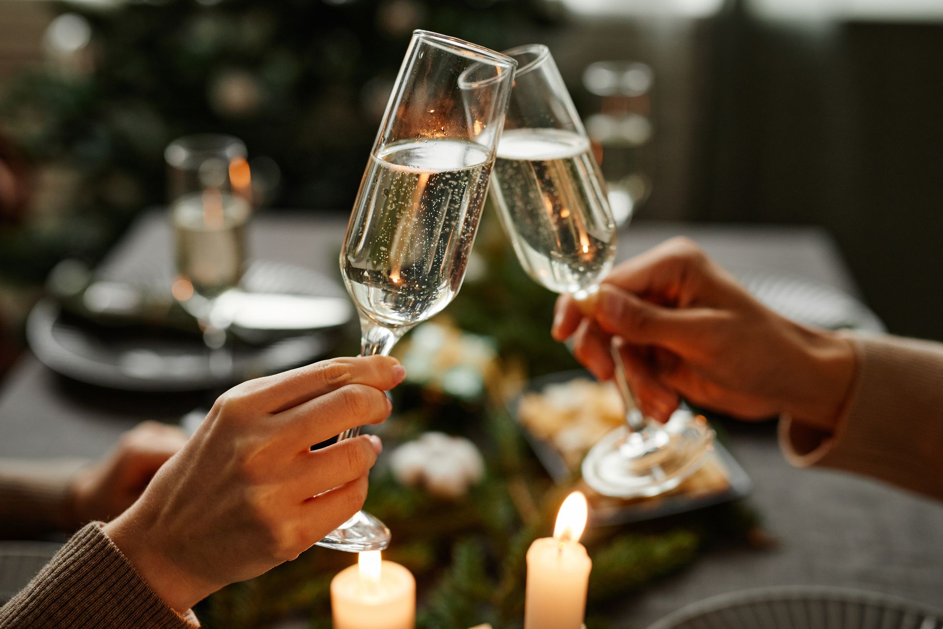 Deux mains qui trinquent avec des flûtes de champagne à une table éclairée aux chandelles.