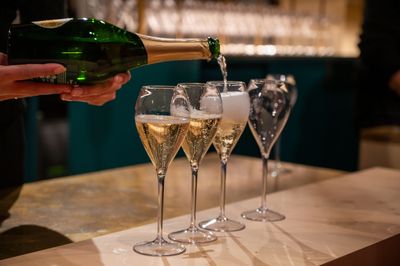 Du champagne est versé dans trois flûtes à un bar, un quatrième verre vide se trouvant à proximité.