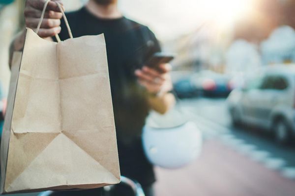 Un hombre sostiene una bolsa de papel marrón y usa un teléfono celular.