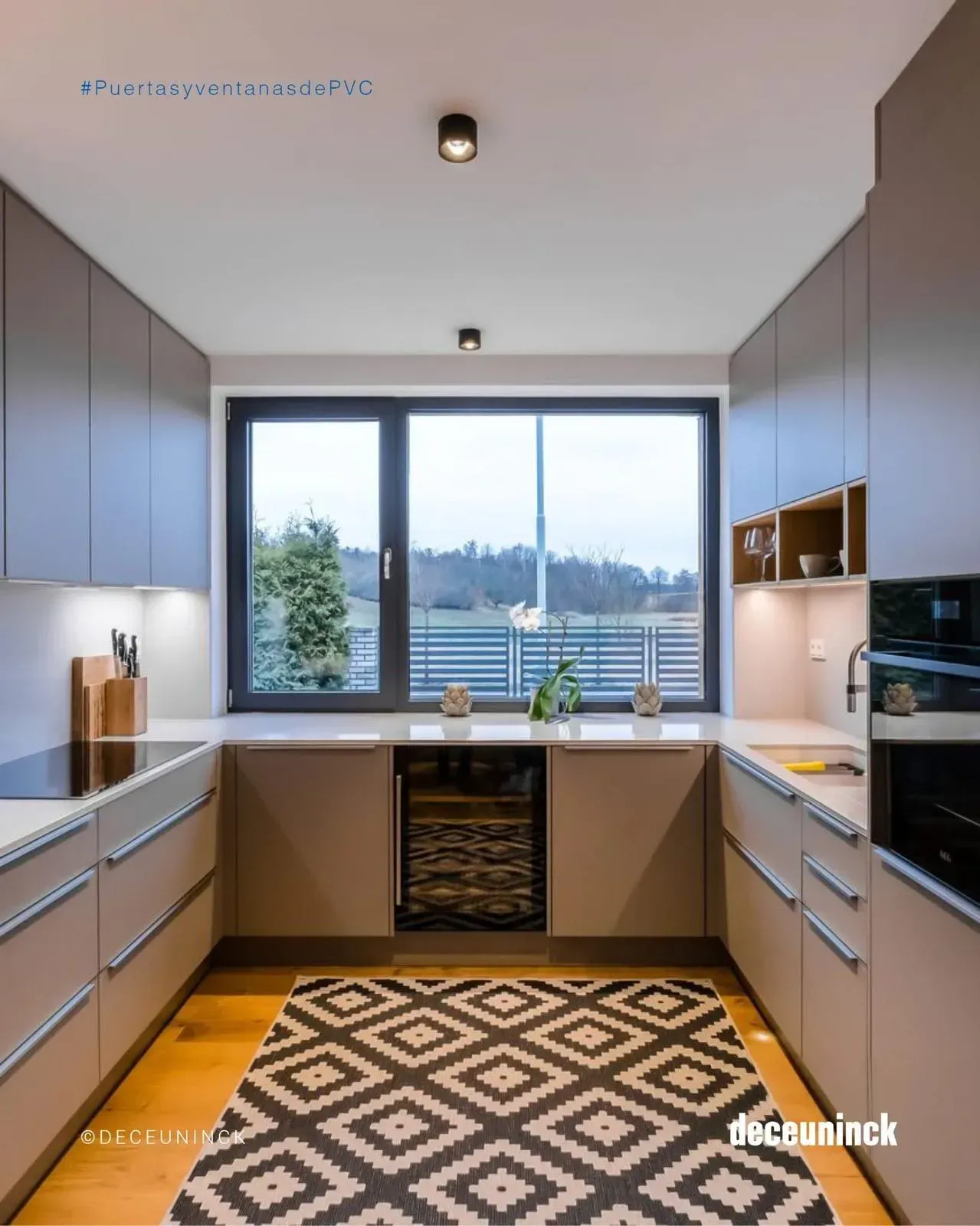 Cocina moderna con armarios grises, una alfombra estampada y una gran ventana con vistas a los árboles