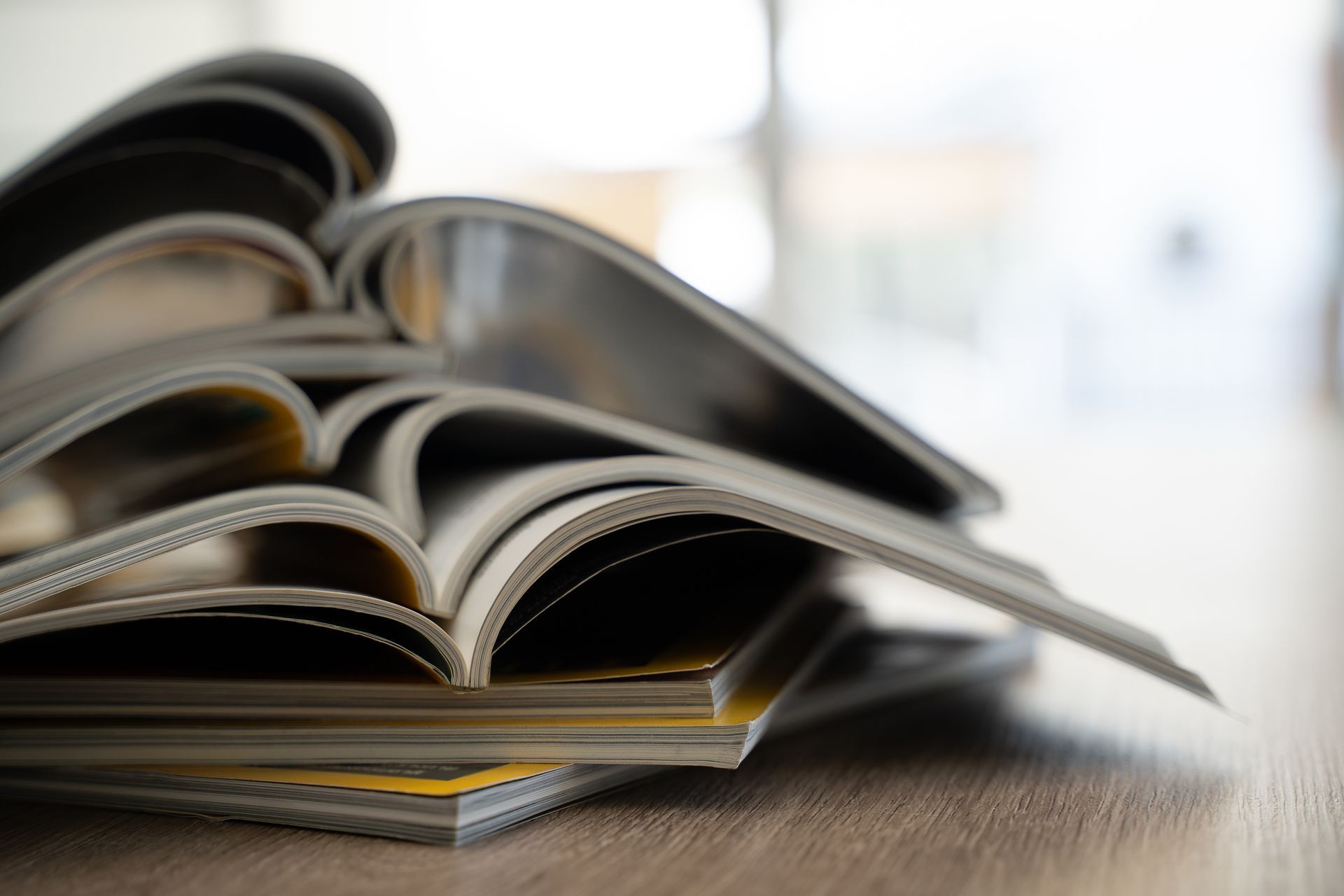 Une pile de magazines ouverts aux pages floues repose sur une surface en bois.