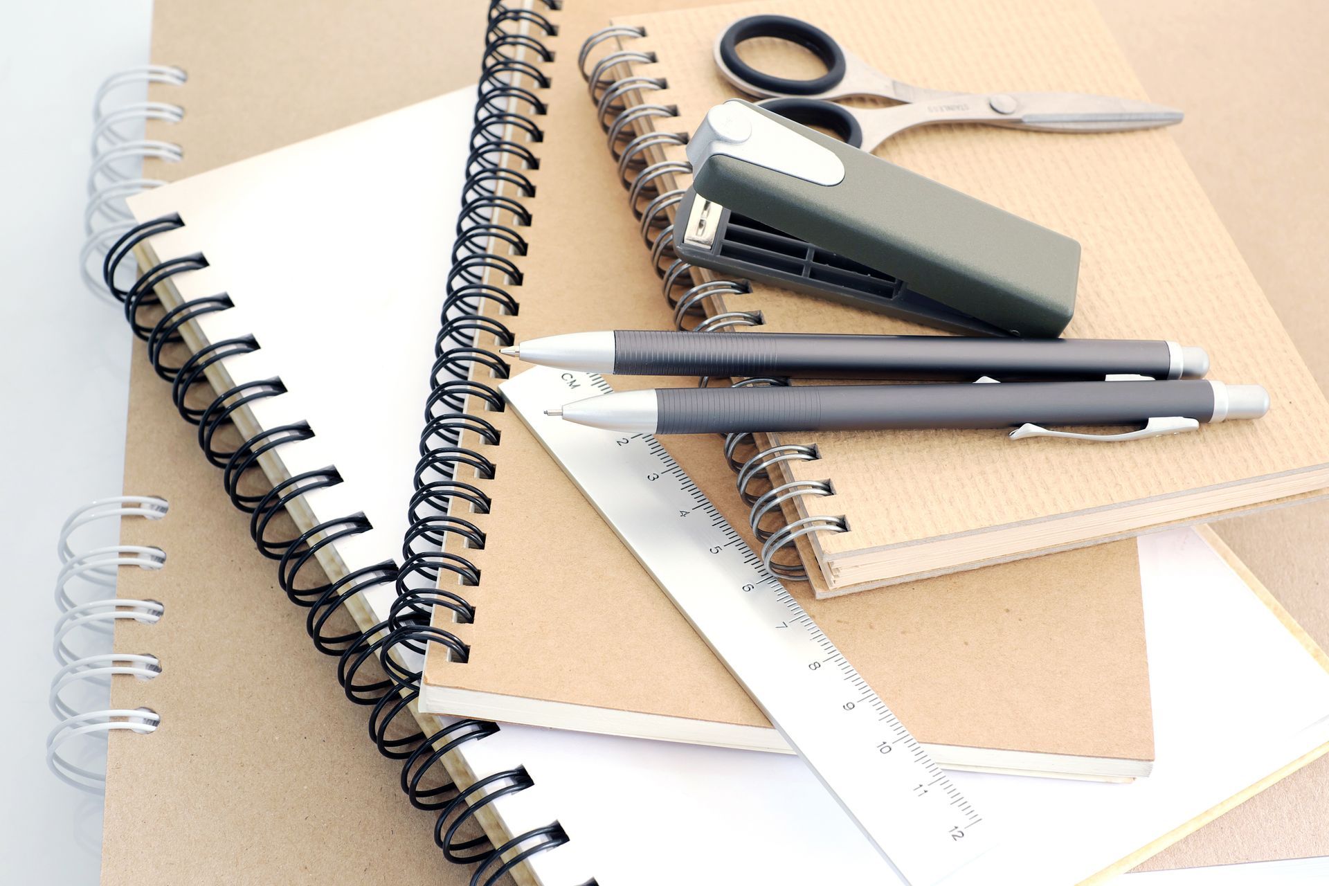 Vue à plat de fournitures de bureau comprenant des cahiers à spirale, une agrafeuse, des ciseaux.