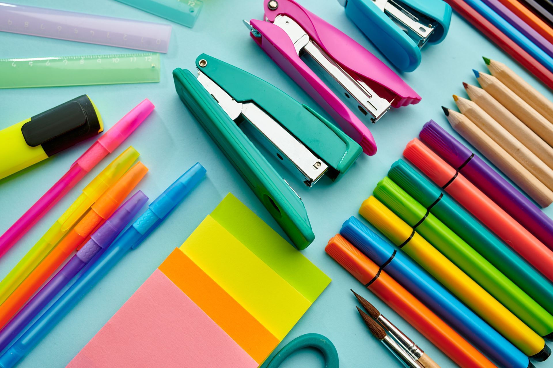 Vue de dessus d'articles de papeterie colorés, notamment des agrafeuses, des marqueurs, des crayons et des notes adhésives.