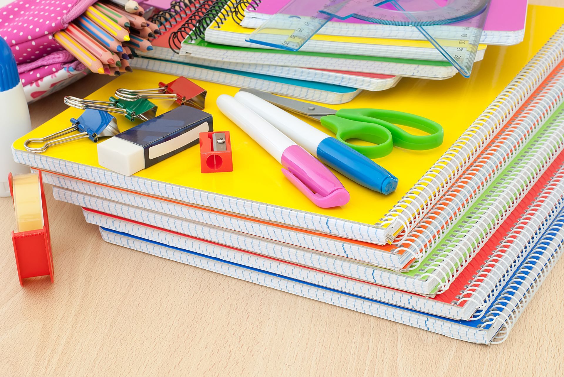 Une pile de cahiers à spirale contenant des fournitures scolaires, notamment des stylos, des ciseaux.