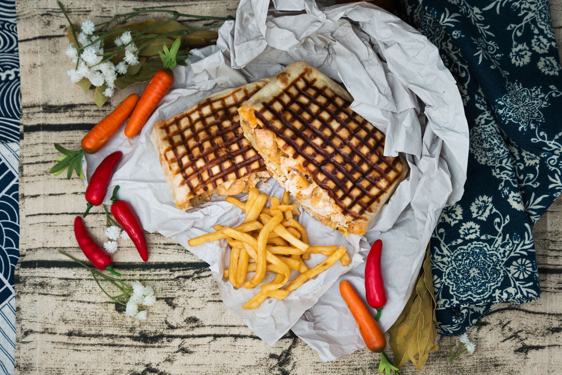 Sandwich grillé, frites et légumes sur une surface en bois rustique avec des accents en tissu.