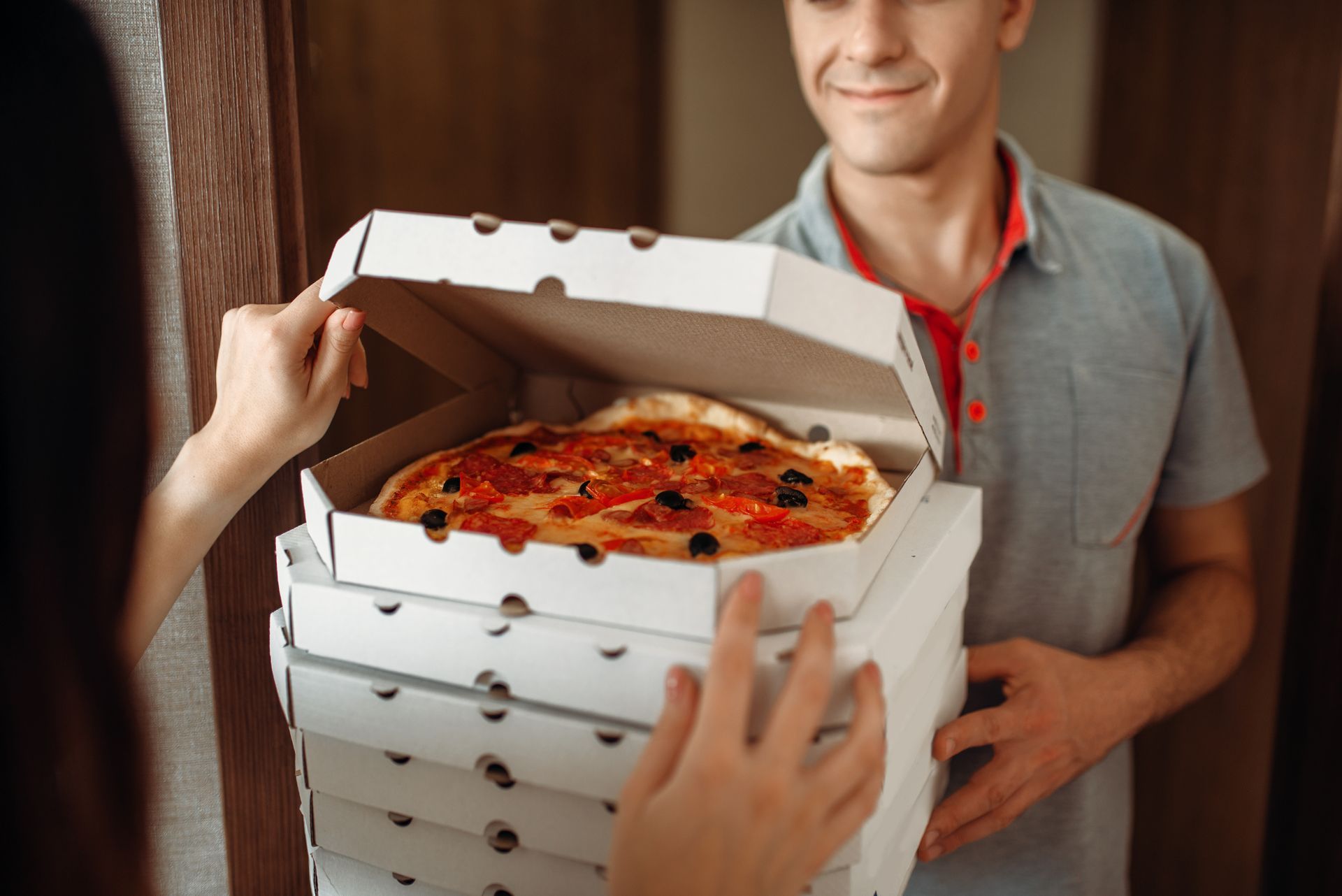 Un livreur de pizza remet une pile de boîtes à pizza à une personne ; une boîte est ouverte, révélant une pizza.