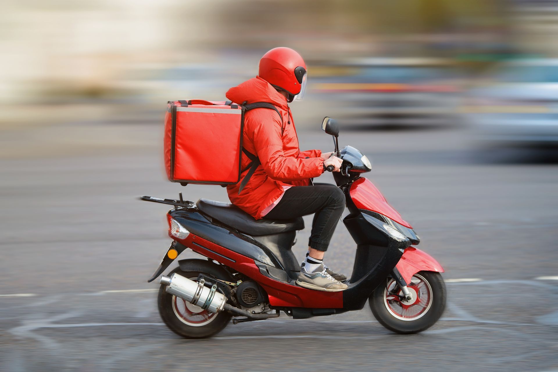 Une personne en rouge conduit un scooter rouge et livre de la nourriture en ville. Arrière-plan flou.