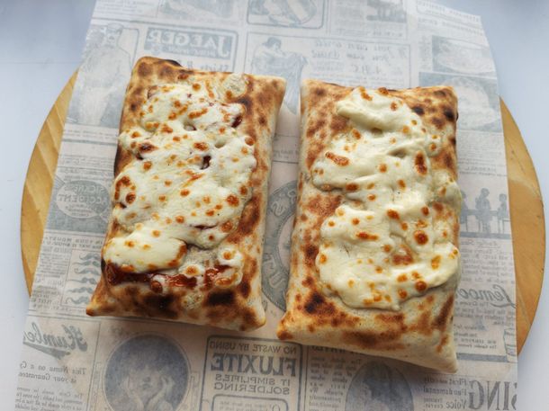 Deux pizzas rectangulaires sur du papier journal, garnies de fromage fondu, sur une planche de service en bois.