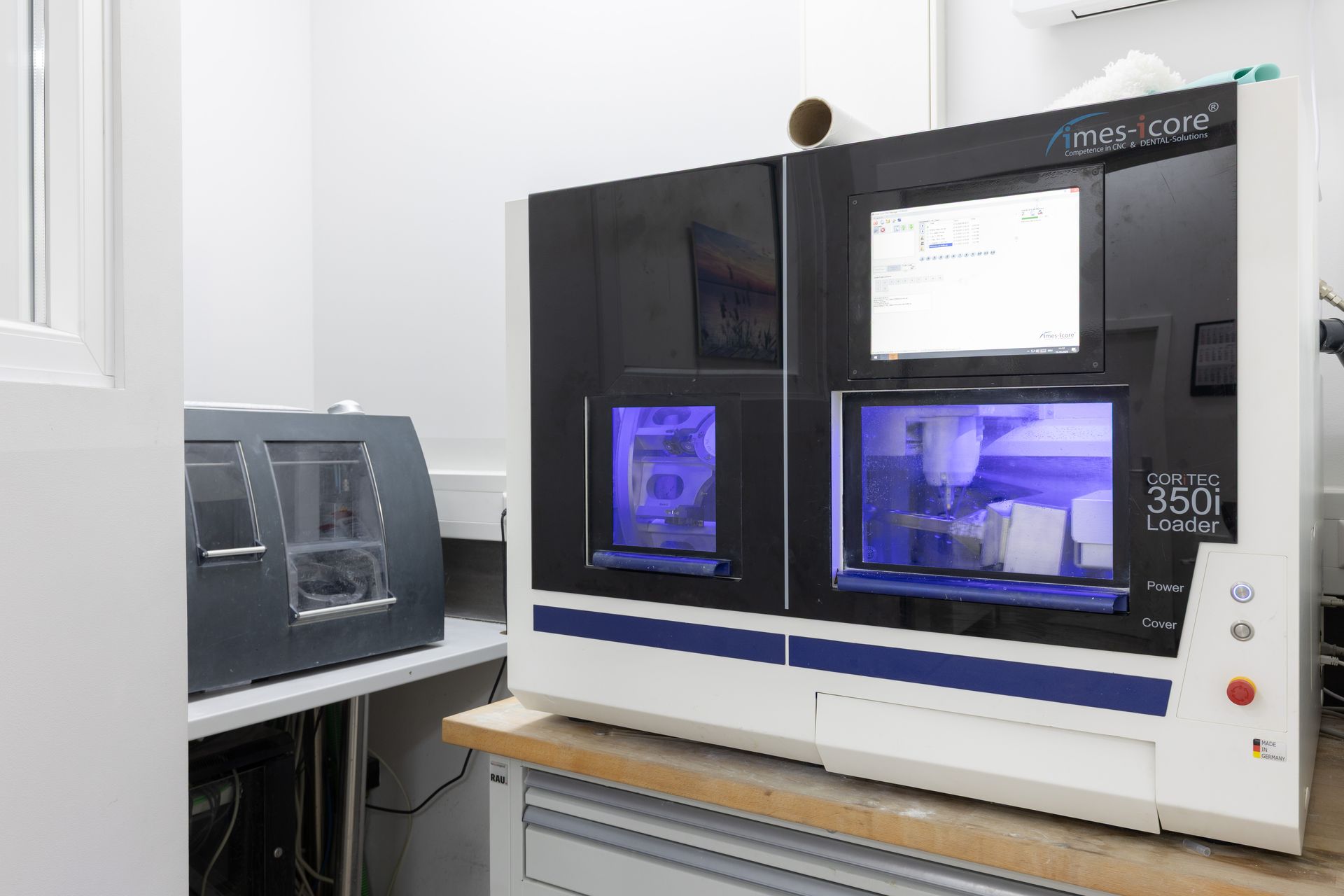 Zahnärztliche Fräsmaschine in einer Laborumgebung, blau-weiße Akzente, mit einem Computerbildschirm.