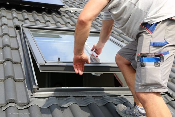 Person arbeitet an einem schrägen Fenster auf einem Dach