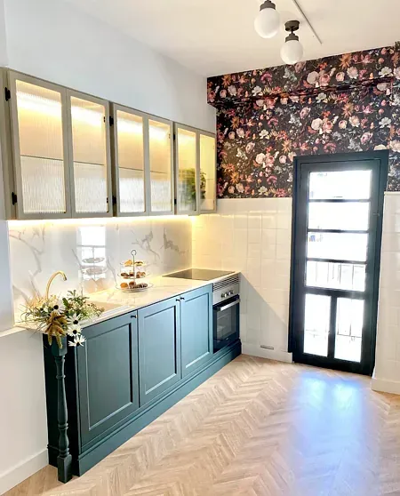 Una cocina con gabinetes verdes y un papel tapiz floral en la pared.