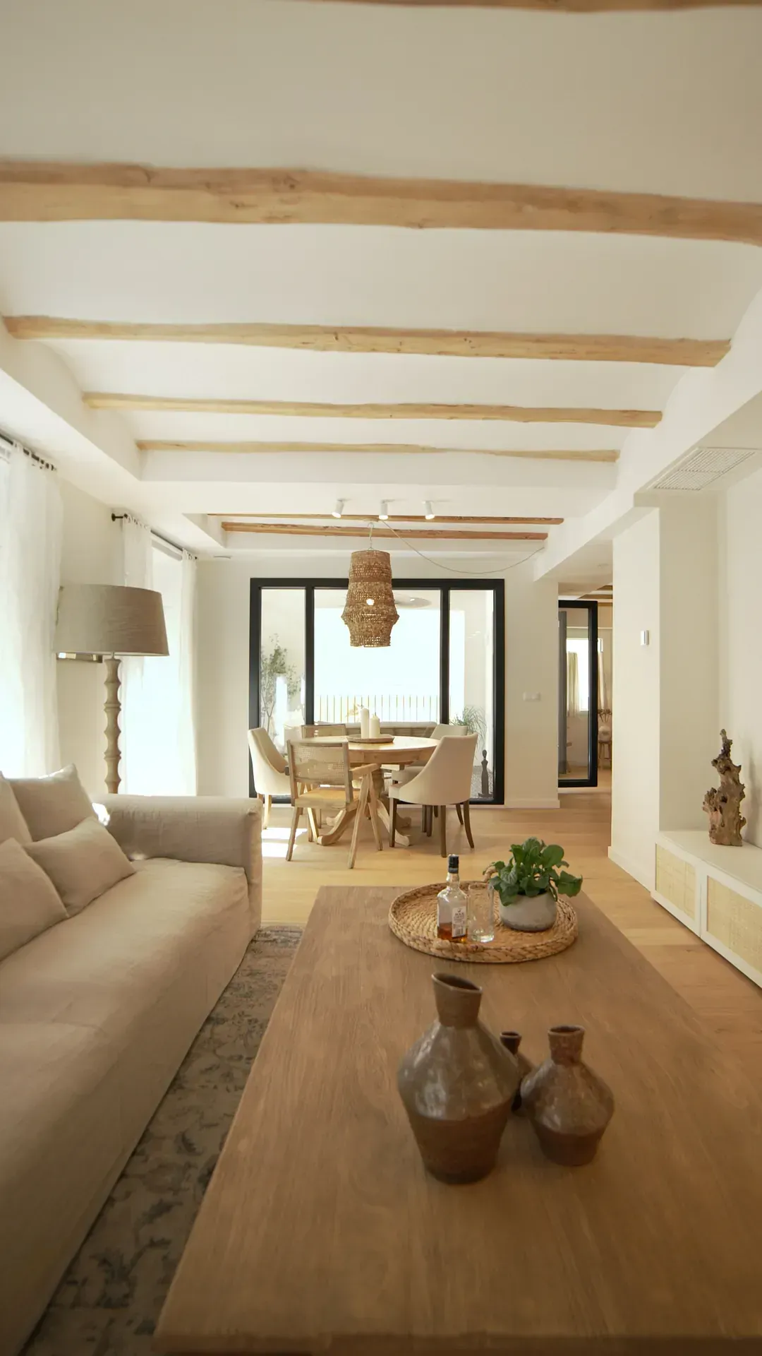 Una sala de estar con un sofá, una mesa, jarrones y un comedor al fondo.