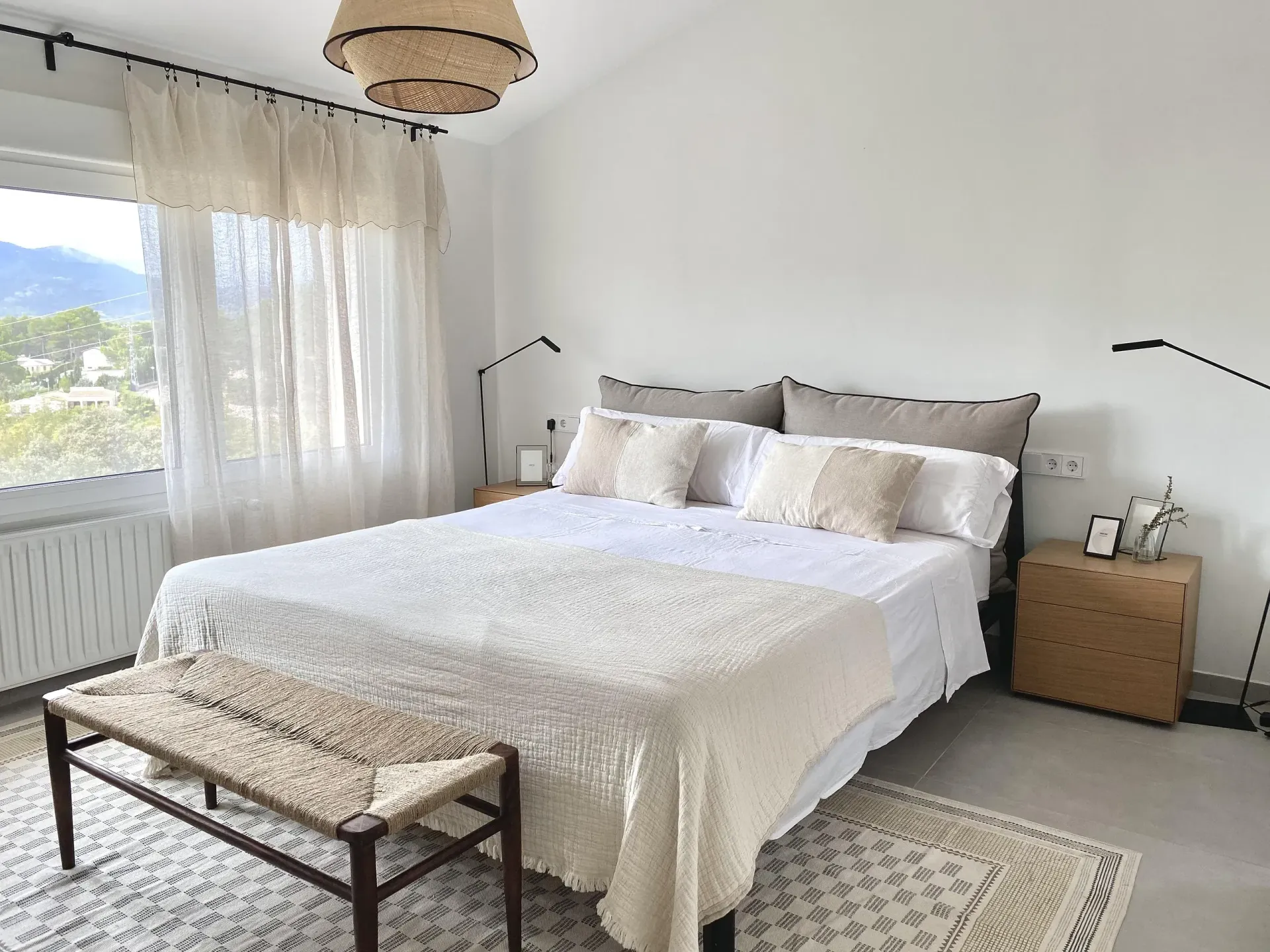 Un dormitorio con una cama, mesitas de noche, un banco y una ventana.