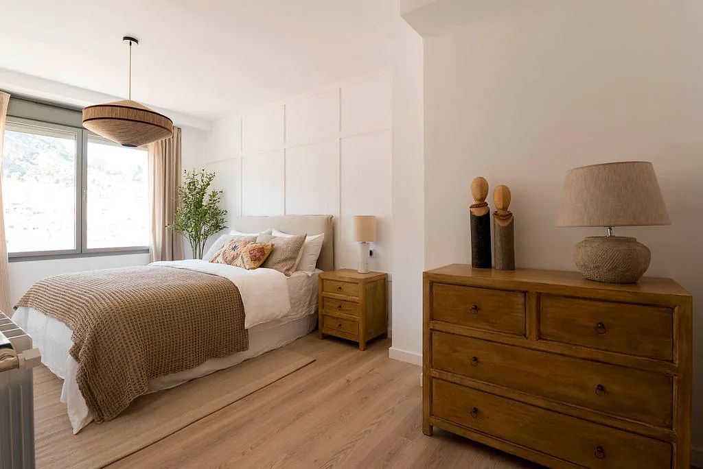 Un dormitorio con cama, cómoda, mesita de noche, lámpara y ventana.