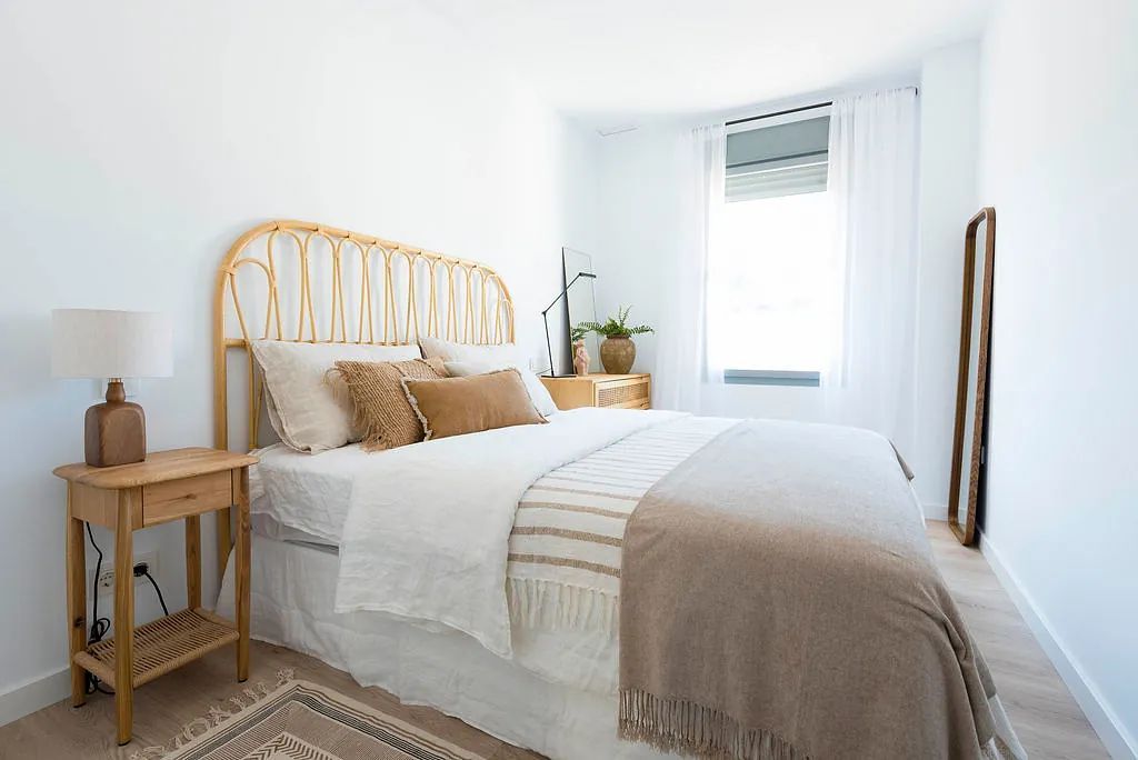 Un dormitorio con cama, mesita de noche, lámpara y ventana.