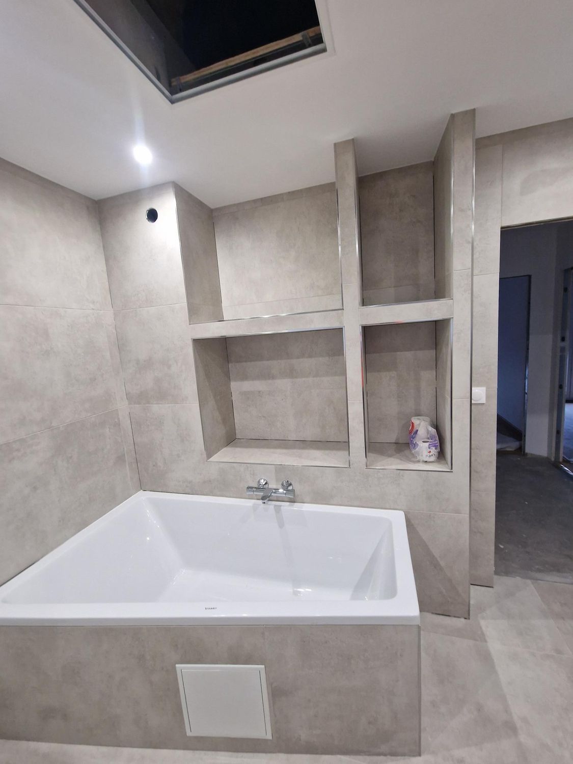 Salle de bains en construction avec baignoire rectangulaire, murs carrelés et étagères intégrées.