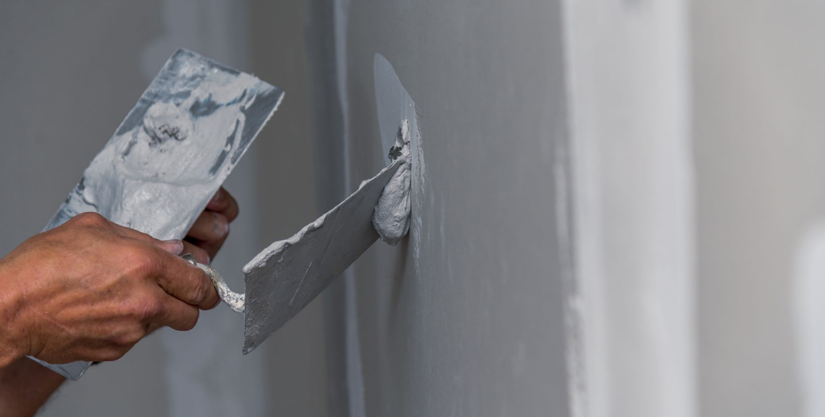 Gros plan d'une main appliquant du mastic sur un mur à l'aide d'un couteau à mastic métallique.